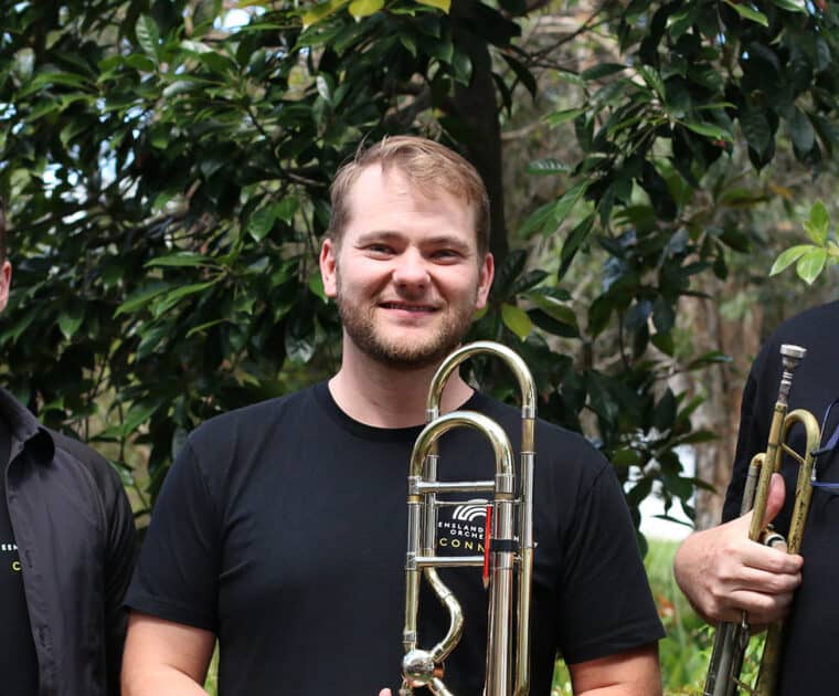 3 members of the Queensland Symphony Orchestra are standing outside holding brass instruments